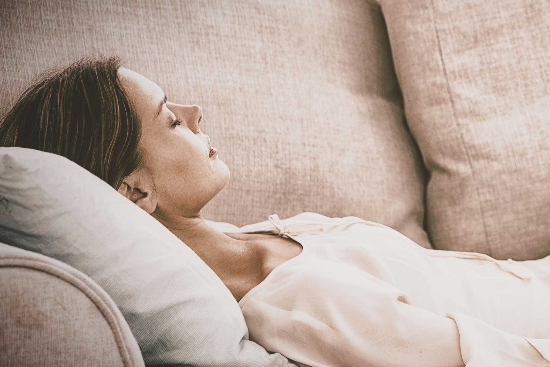 Eine Frau liegt mit geschlossenen Augen auf einem Sofa